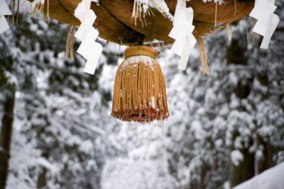 The tassels of the sacred rope at Oyama Shrine, covered in snow. A snow-covered forest spreads out in the background.