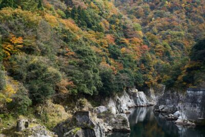 The tranquil river flowing through the valley of Jinzukyo Gorge, surrounded by mountains and rock faces dyed in autumn colors