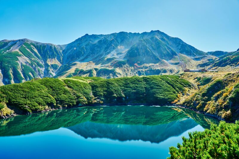 Mt. Tateyama's Oyama soars against the blue sky, while the mountain ridges and autumn foliage are vividly reflected in Mikuriga Pond in the foreground.