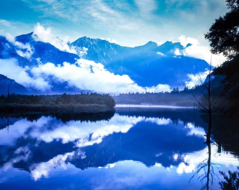 The Hotaka Mountain Range viewed from Taisho Pond in Kamikochi. A landscape photograph capturing clouds and mountains reflected on the lake's surface.