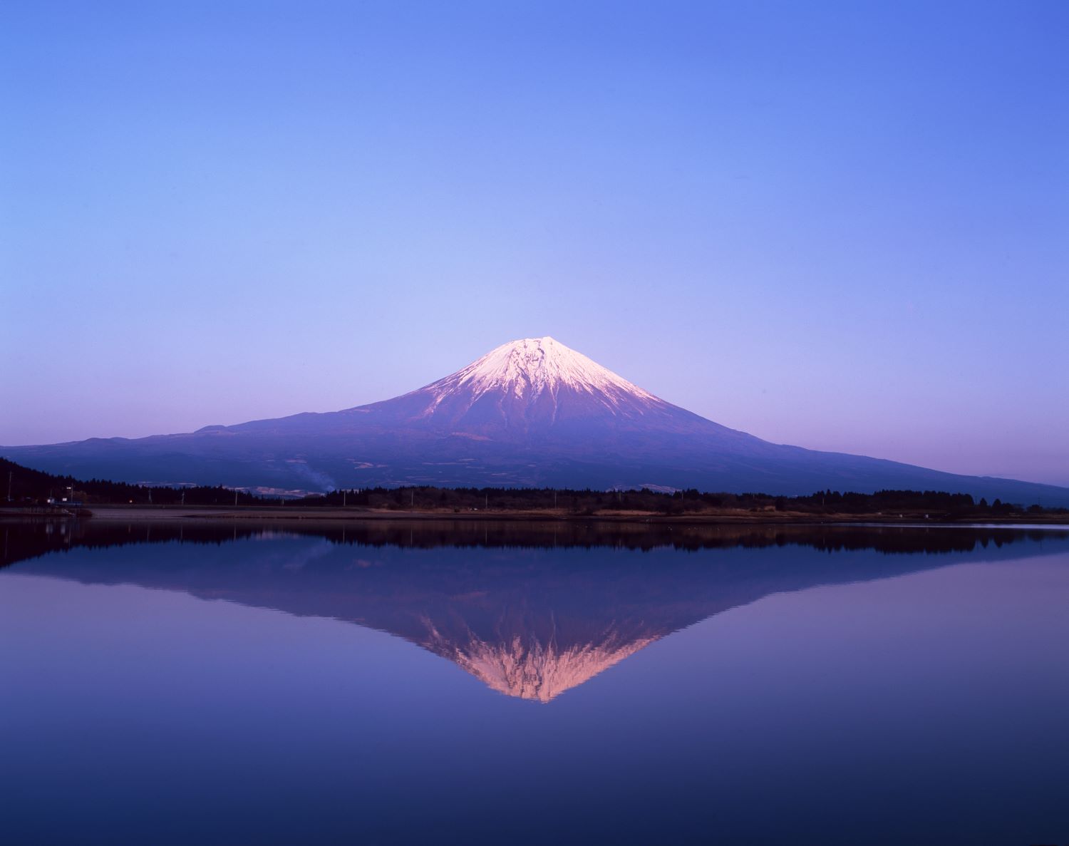A landscape photograph capturing Mount Fuji perfectly reflected on the surface of Lake Tanuki against the backdrop of the dawn sky.