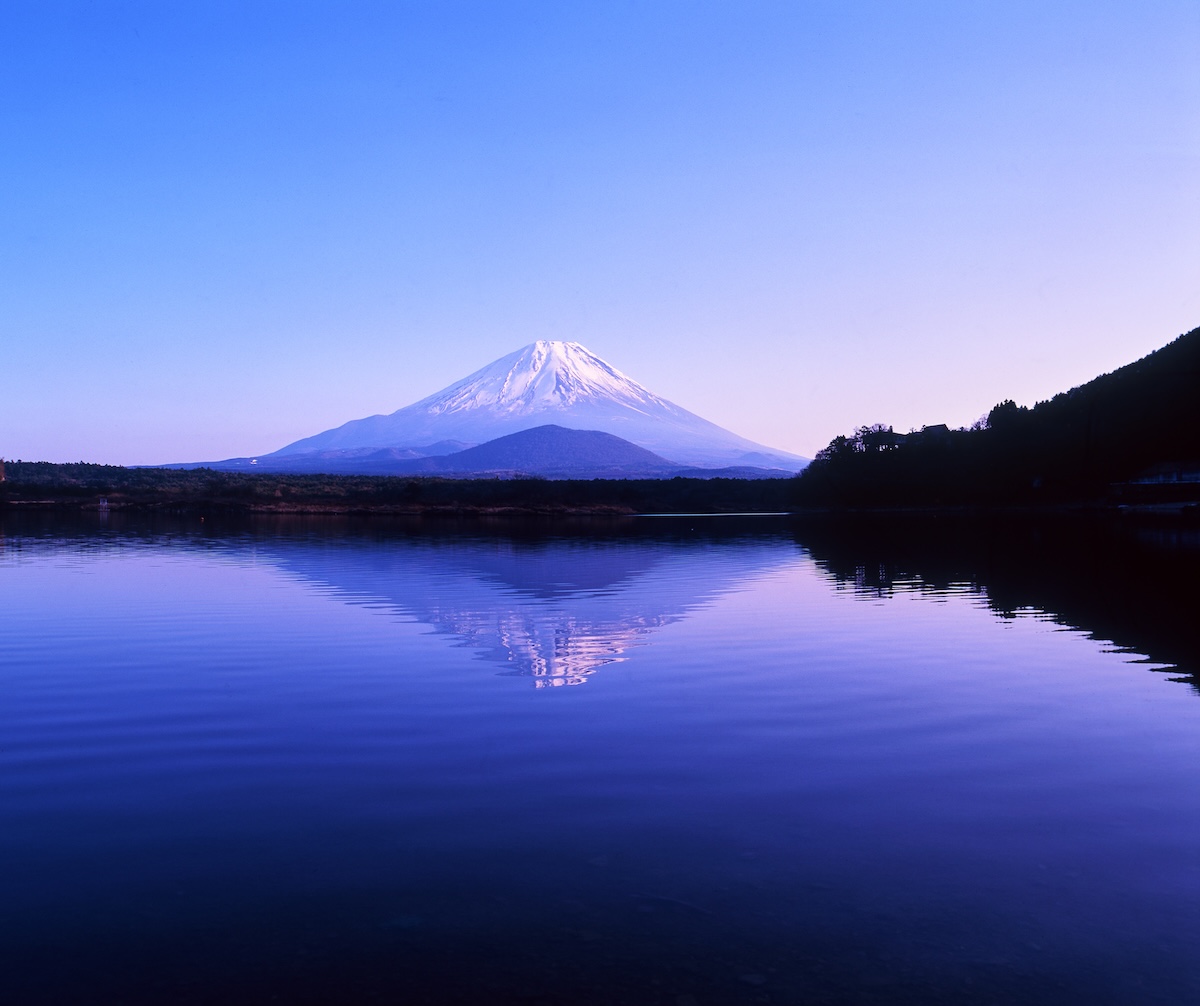 Mount Fuji reflected upside down in Lake Shōjiko. The mountain dyed in the morning glow sky and its reflection on the tranquil lake surface.