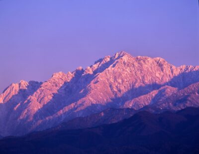 In the evening's oblique light, Mount Tsurugi, cloaked in snow, glows crimson-purple in the distance.