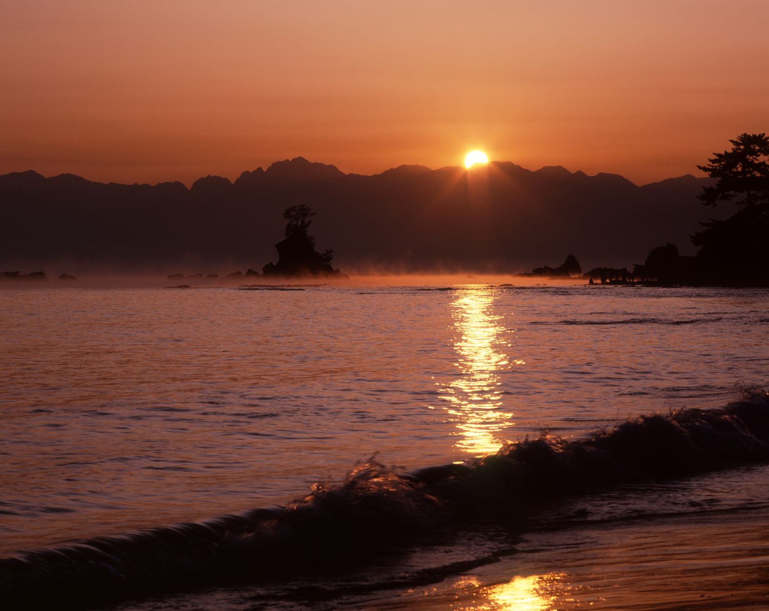 Sunrise viewed from Amahare Beach. The sun rising above the ridgeline of Mt. Tateyama and the path of light reflecting on the sea surface create a striking scene.