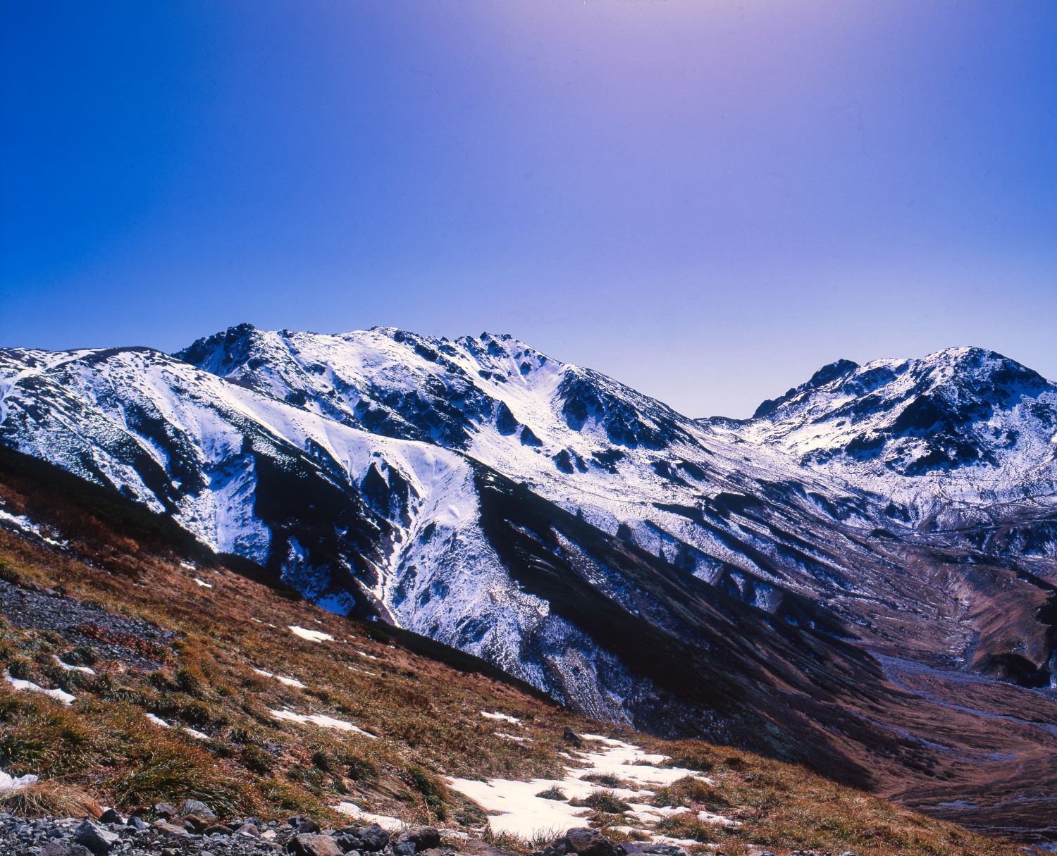 Against a backdrop of blue skies, the snow-capped Mt. Tateyama mountain range stretches its ridgeline across the early winter landscape.