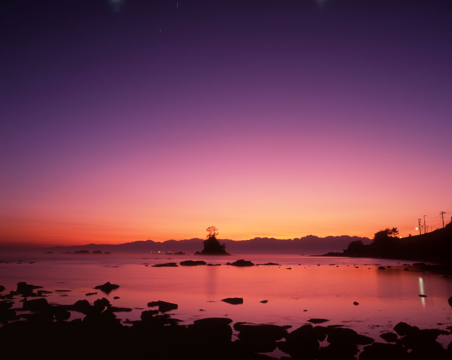 The scenery of Amahare Beach before dawn. A striking photograph of the sky and sea dyed from purple to vermilion, with the silhouettes of rocks.