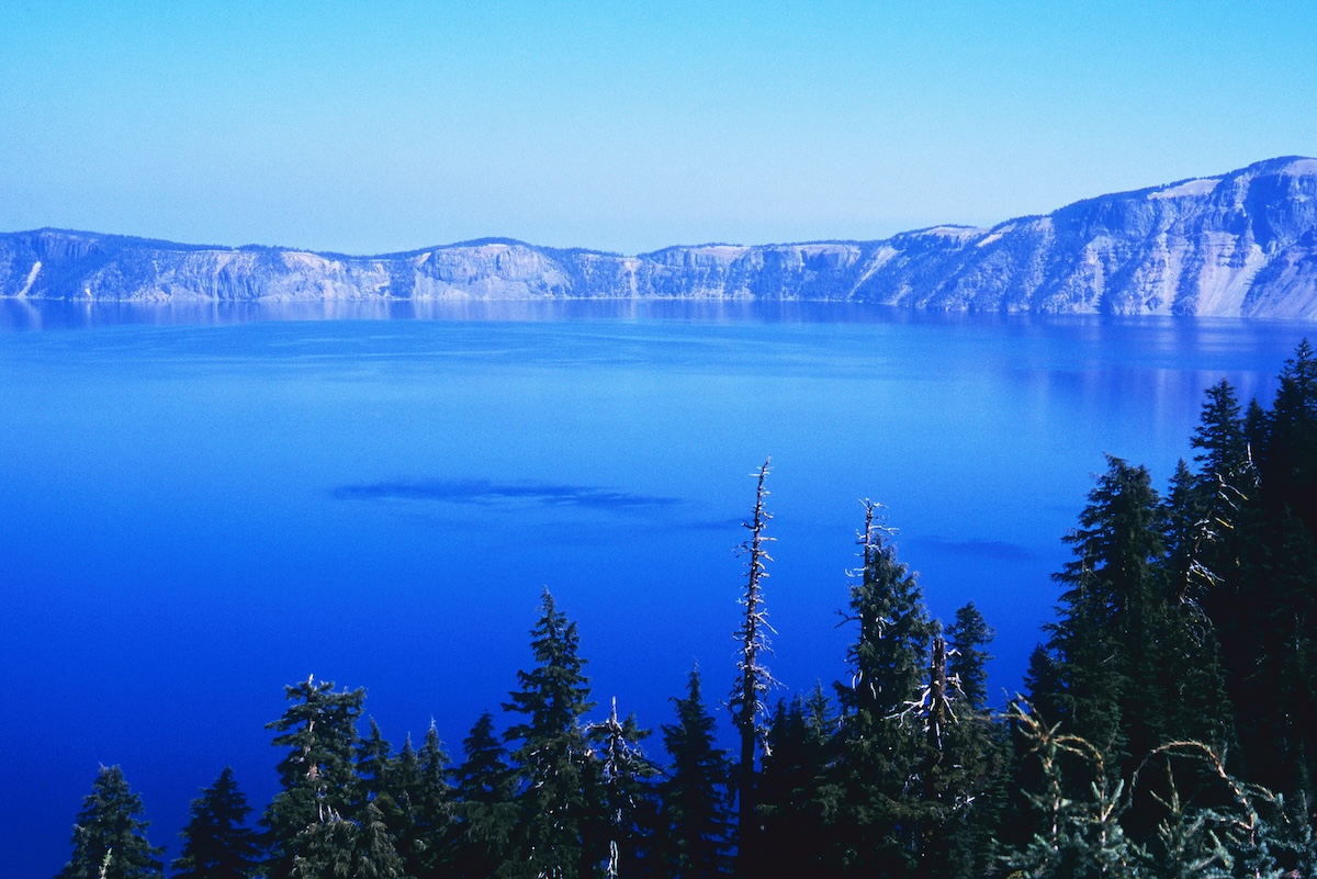 The still lake surface of Crater Lake on a windless morning and the reflections of the surrounding mountains
