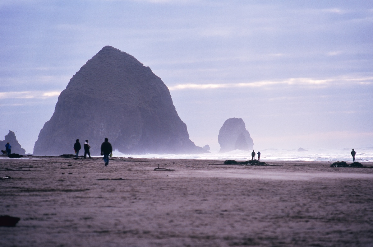 Haystack Rock floating in the morning mist and people walking along the coast