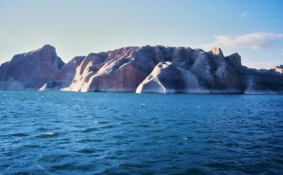 The reddish-brown rock walls of Lake Powell and the blue lake surface illuminated by the light before dusk
