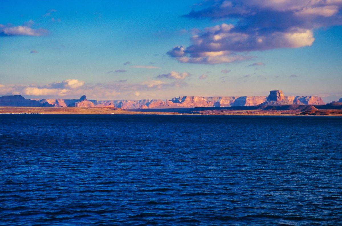 The rock walls of Lake Powell stained red by the evening light and the calm lake surface