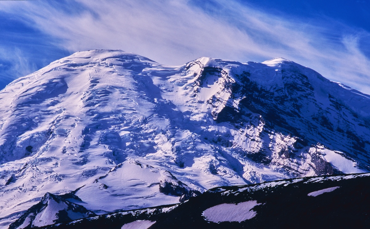 Under the blue sky, Mount Rainier's snow and rock face illuminated by the summer sun