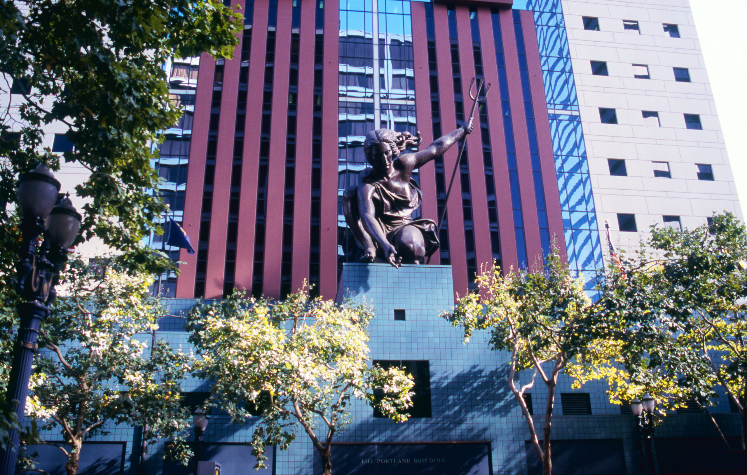 Portlandia, the large bronze statue standing atop the entrance to Portland City Hall. She holds a trident in her left hand and extends her right hand, gazing down at us.