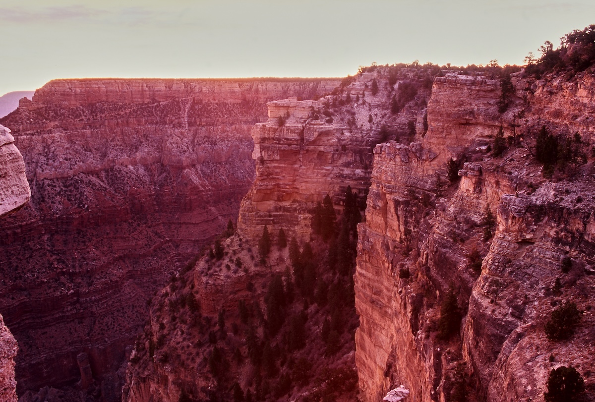 The Grand Canyon's cliffs and layered rock faces, dyed crimson by the setting sun