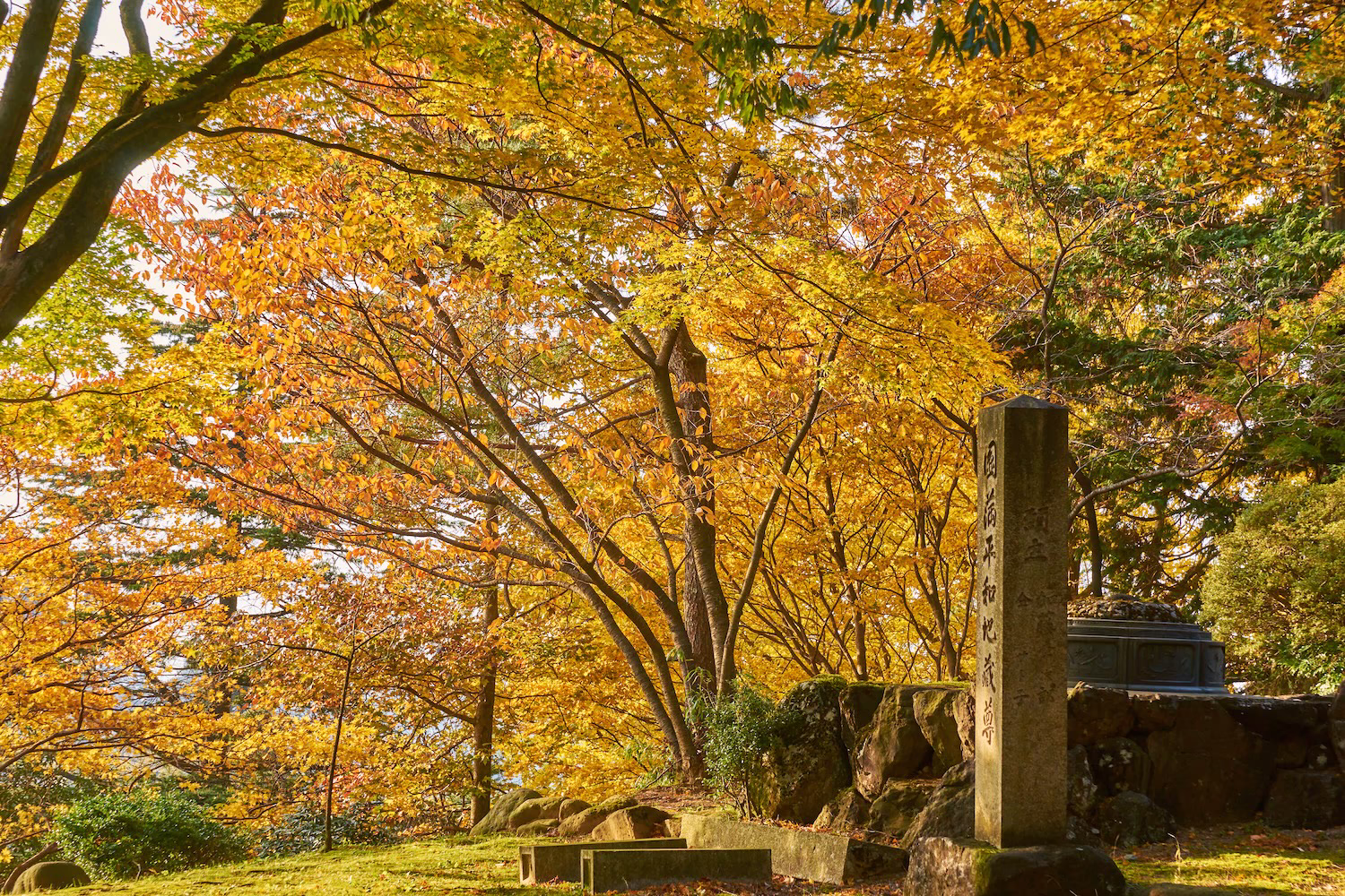 The stone monument and autumn trees enveloped in the autumn foliage at Jike Park in Toyama City