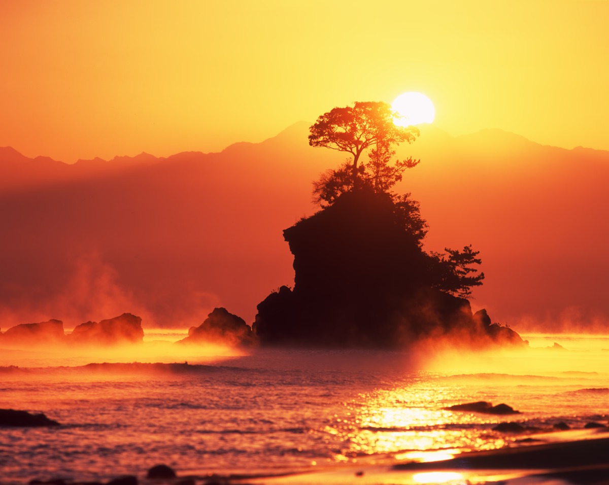 A higher sun rising behind Onna-iwa, illuminating sea smoke and the ocean in golden light at Amaharashi Coast.